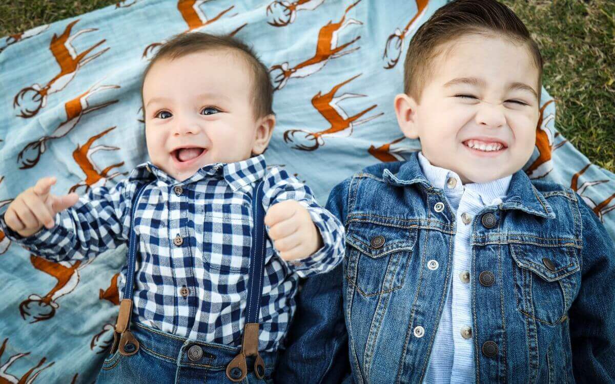 Two boys laying on the blanket on the grass and smiling