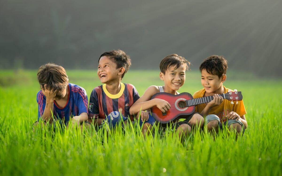 Four boys sitting in a field wit a guitar and smiling